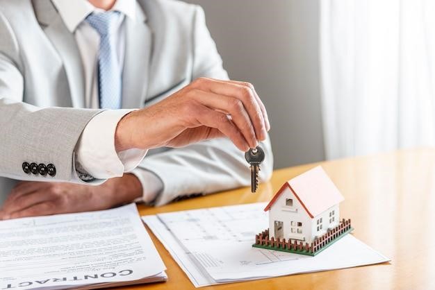 Pessoa segurando as chaves de uma casa e uma modelo de casa de brinquedo na mesa, representando a tentativa bem sucedida de um advogado em reaver imóvel leiloado por dívida condominial.