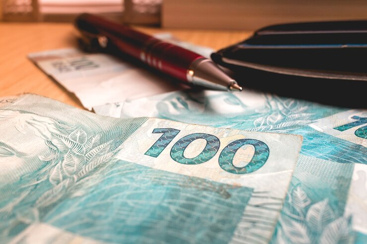 Dinheiro brasileiro em foto perto de uma caneta e uma carteira, representando a busca por um financiamento para dívida condominial