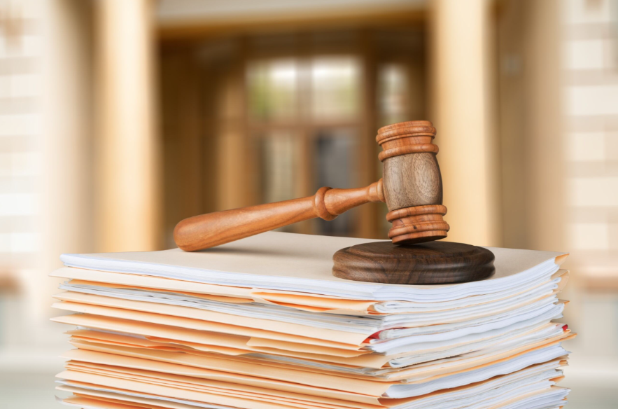 Malhete em cima de uma pilha de documentos de penhora online. Você sabia que, mesmo sem aviso prévio, a sua conta bancária pode ser bloqueada devido a uma penhora online por um processo de dívida condominial?