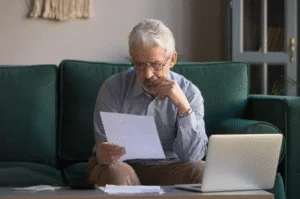 Homem de meia-idade sentado no sofá analisando as dívidas condominiais, pensando em uma solução para evitar um leilão de imóvel.